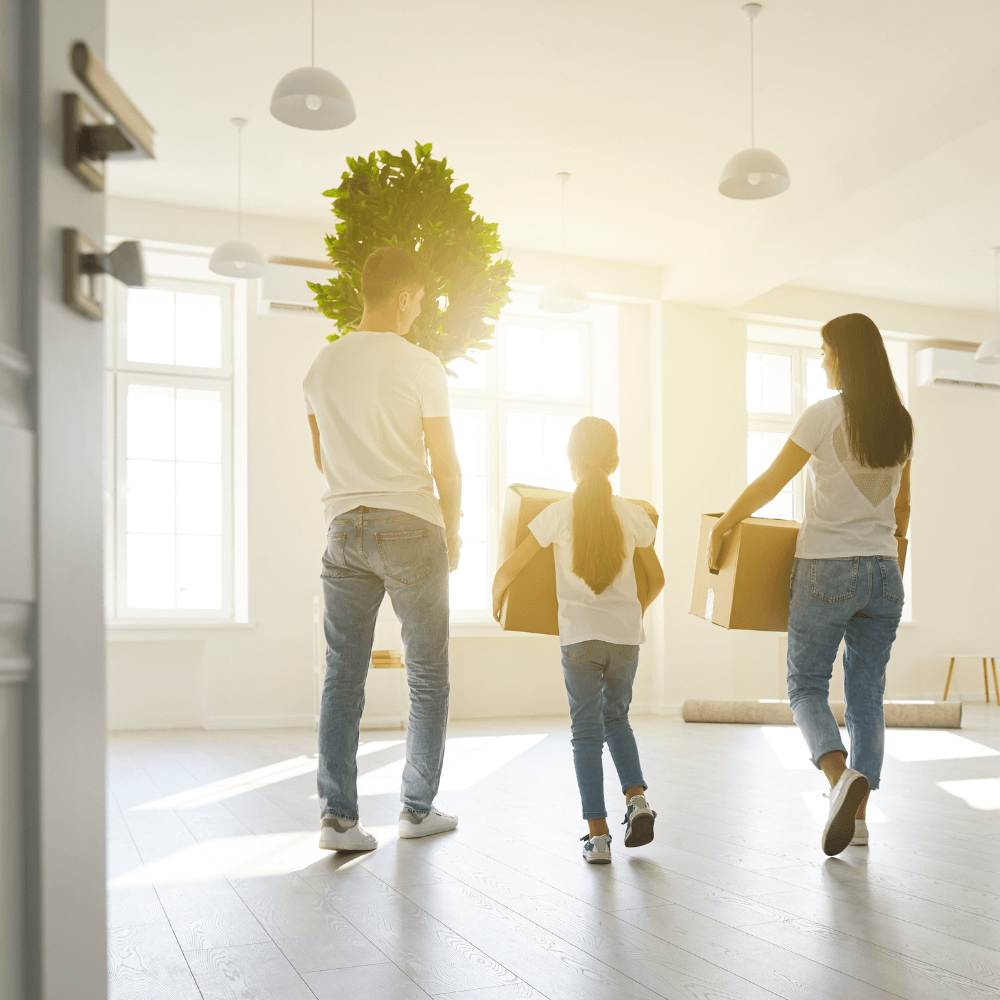 Photo d'une famille de dos composée des deux parents et de leur fille entrain de porter des cartons pendant leur emménagement