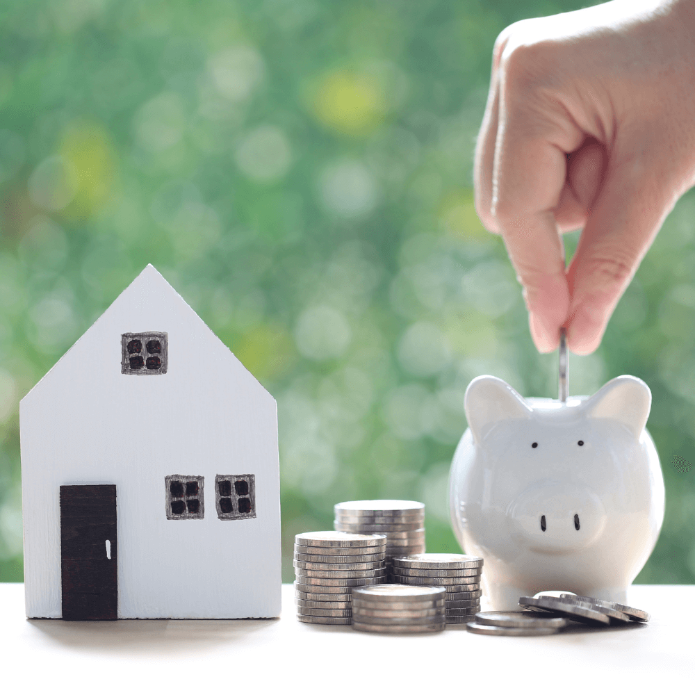 Photo d'une maisonnette blanche en bois, d'un tas de pièces de monnaie et d'une tirelire en forme de cochon blanche
